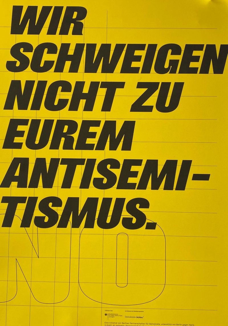 "Wir schweigen nicht zu eurem Antisemitismus" schwarze Schrift auf gelbem Hintergrund.