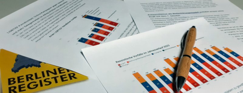 auswertung23_20240410_223241 Blätter Papier auf einem Tisch, darauf Stift, mehrere Grafiken und Text zu Rassismus, Antisemitismus, Queer, Logo Register